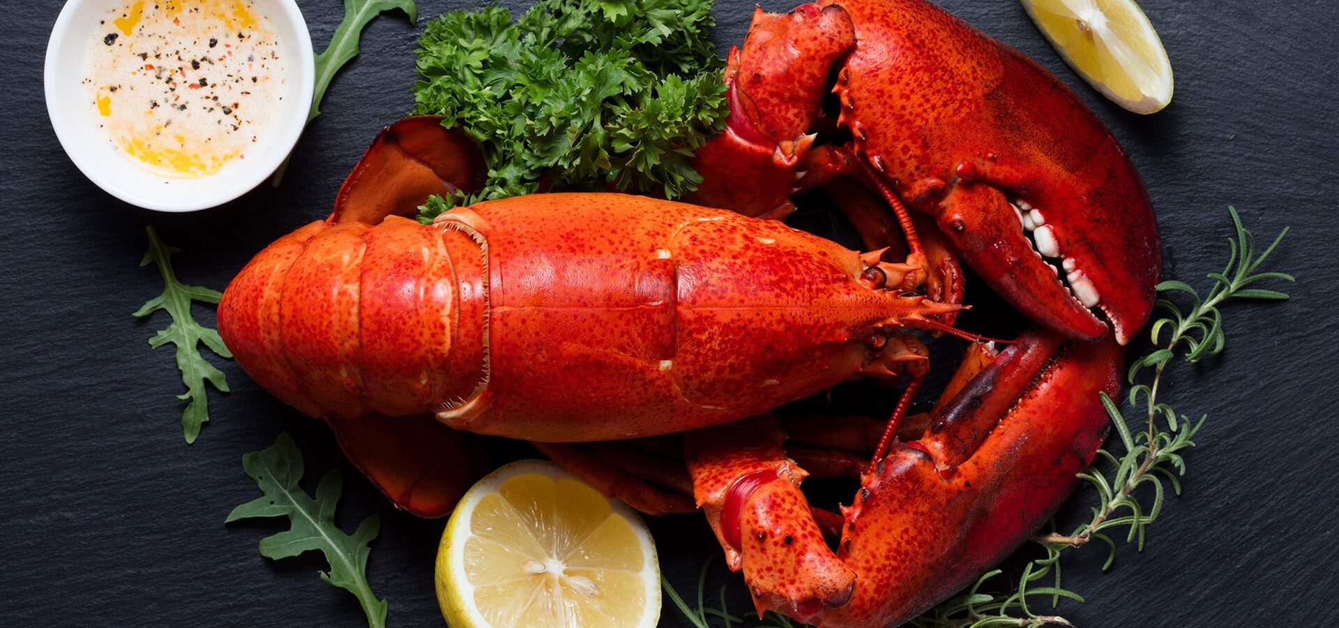 Whole cooked lobster with lemon and drawn butter on a rustic black stone background